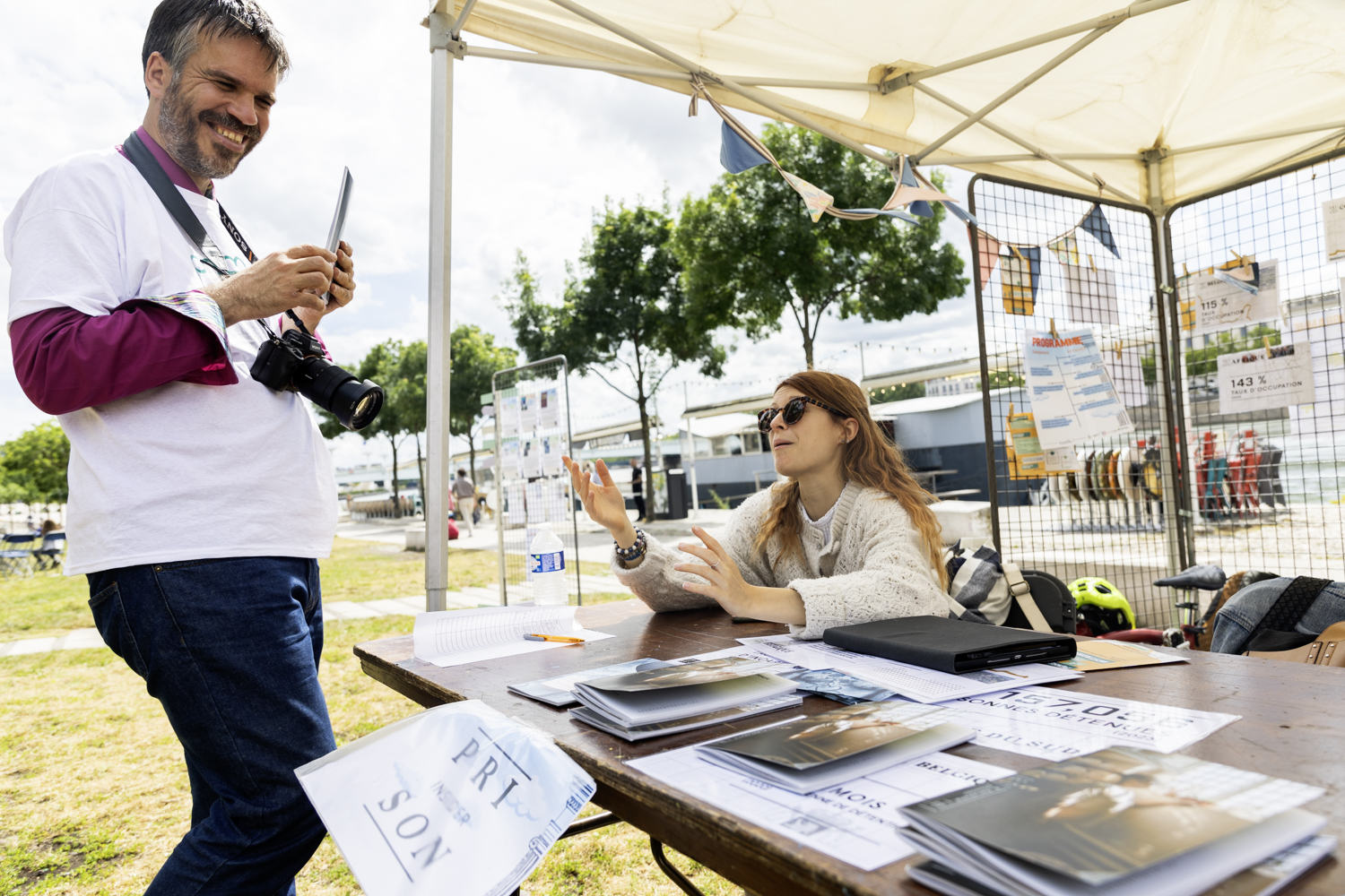 Sous un chapiteau, un homme debout rit devant le stand d'une femme assise